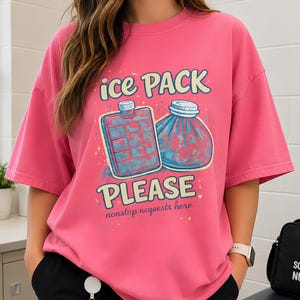 May include: A bright pink t-shirt featuring a graphic of an ice pack and a cold compress with the text "ice PACK PLEASE" and "nonstop requests here" in a playful font. The design includes small colorful speckles surrounding the medical items.