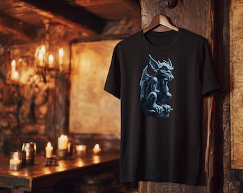 May include: Black t-shirt featuring a detailed illustration of a blue gargoyle statue. The gargoyle is depicted with its chin resting on its hand, giving a thoughtful expression. The shirt is hanging on a wooden hanger.