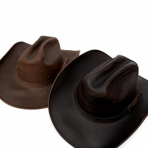 May include: Two cowboy hats with wide brims and pinched crowns. One hat is a medium brown shade, while the other is a darker, deep chocolate brown. Both hats feature a smooth, matte finish and a matching band around the base of the crown.