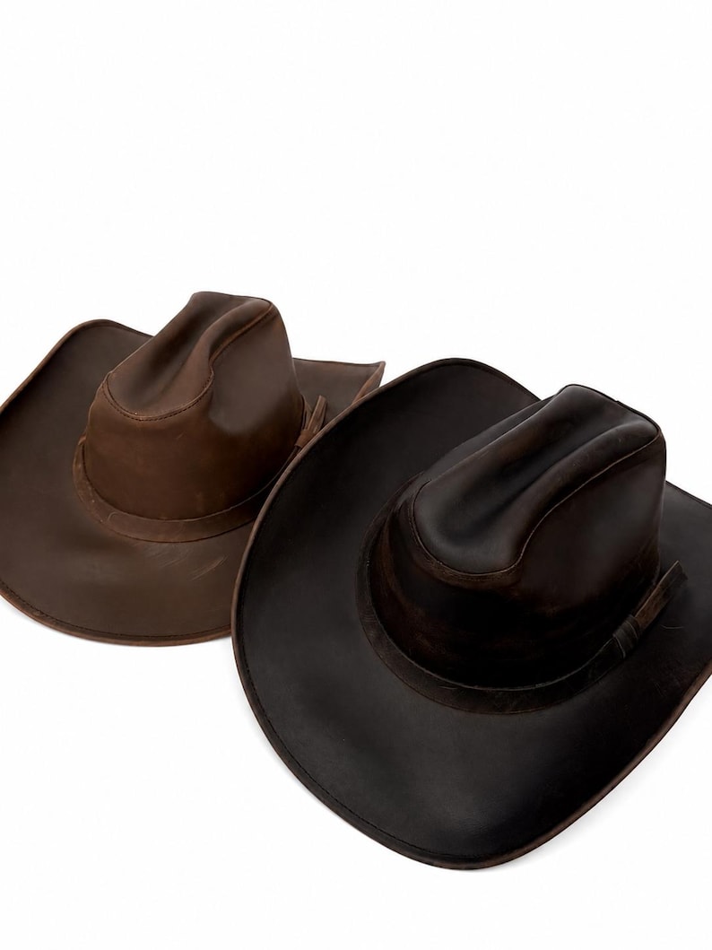 May include: Two cowboy hats with wide brims and pinched crowns. One hat is a medium brown shade, while the other is a darker, deep chocolate brown. Both hats feature a smooth, matte finish and a matching band around the base of the crown.