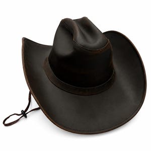 May include: A dark brown cowboy hat with a wide, curved brim and a pinched crown. The hat features a matching dark brown band around the base of the crown and a thin, adjustable brown chin cord with a small black plastic toggle for tightening.