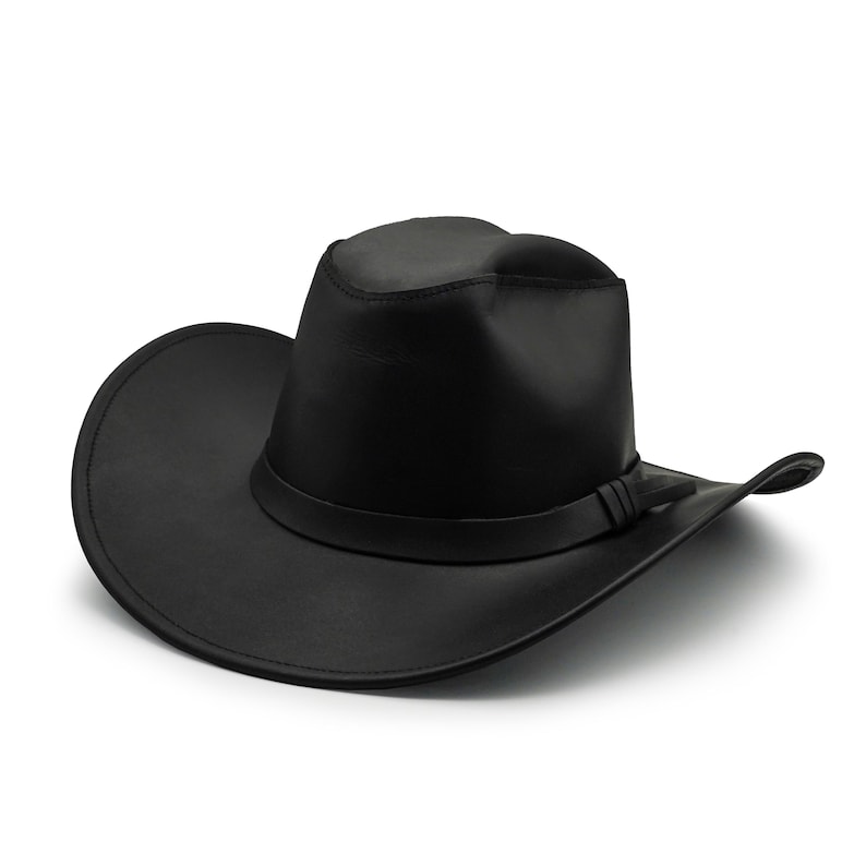 May include: A solid black cowboy hat featuring a structured crown with a central crease and a wide, curved brim. The hat includes a matching black band wrapped around the base of the crown, finished with a small, simple knot detail on the side.