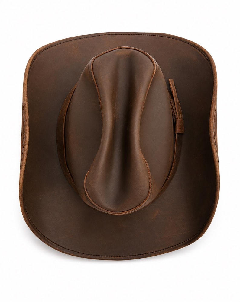 May include: A top-down view of a dark brown leather cowboy hat featuring a pinched crown and a wide, curved brim. The hat includes a matching leather hat band wrapped around the base of the crown, with visible stitching along the brim edge.