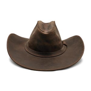 May include: A dark brown leather cowboy hat with a distressed finish, featuring a pinched crown and a wide, curved brim. A matching leather band wraps around the base of the crown, secured with a small, simple leather knot detail on the side.