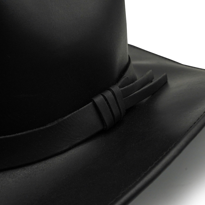 May include: A black hat with a smooth, matte finish and a wide brim. The hat features a matching black leather-like band wrapped around the base of the crown, secured with a simple knot detail on the side, creating a clean and uniform appearance.