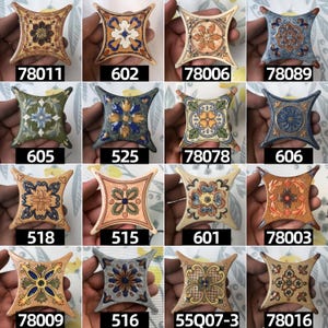 May include: A collection of decorative ceramic tiles with various floral and geometric patterns in shades of blue, orange, brown, and green. Each tile has a unique design and is labeled with a number. The tiles are square with a slightly curved shape.