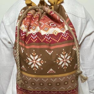 May include: Drawstring backpack featuring a geometric pattern in brown, red, and white. It has a rope drawstring and yellow fabric straps. The bag's design has a Southwestern or tribal aesthetic.