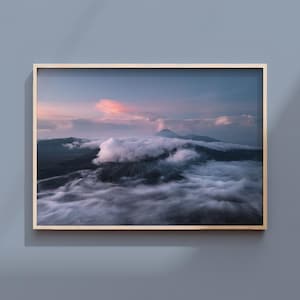 May include: A rectangular wall art print in a light wood frame featuring a landscape photograph of a mountain peak partially obscured by thick, low-hanging white clouds under a soft pink and blue twilight sky at dusk or dawn.