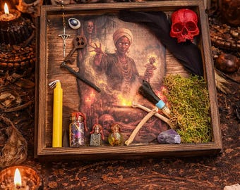 Puede incluir: Una exhibición enmarcada en madera con una imagen central de una mujer con un pañuelo en la cabeza, rodeada de velas, una calavera roja y varios objetos rituales. Incluye pequeñas botellas, una llave y un colgante de cruz. El tema general es místico y espiritual.
