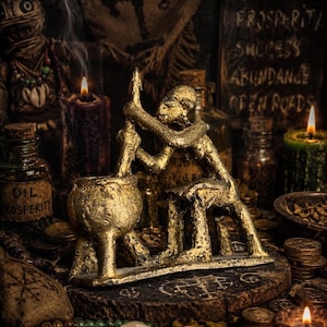 Puede incluir: Una estatua dorada de una persona moliendo hierbas, rodeada de velas, botellas y monedas. La escena incluye una muñeca vudú, un letrero con texto y varios objetos rituales. El tema es la espiritualidad y el misticismo.