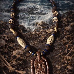 May include: A handcrafted necklace with a carved pendant featuring a face, skull beads, and woven elements. The necklace is made of brown and blue beads. The background shows a beach with skulls and bones.