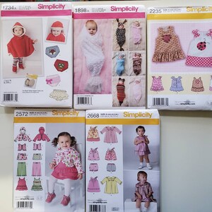 May include: Five different Simplicity sewing patterns for baby clothes. The patterns are for sizes newborn to 24 months. The patterns include a variety of styles, such as dresses, rompers, and tops. The patterns are all on a white background with colorful illustrations.
