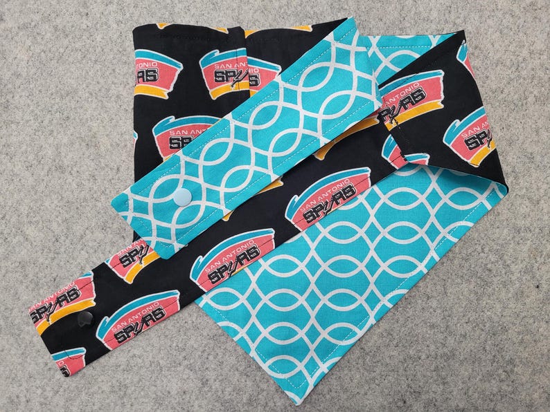 May include: A set of reusable fabric items featuring a black background with the San Antonio Spurs logo in red, yellow, and teal. Accents include teal fabric with a white geometric pattern. The set includes a variety of sizes and shapes.