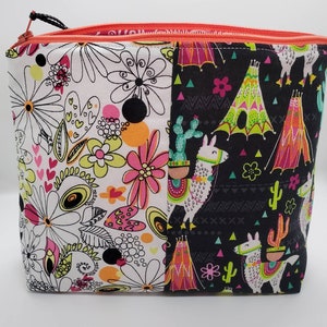 May include: A black and white zippered pouch with a floral design on one side and a llama and teepee design on the other side. The pouch is made of fabric and has a zipper closure.