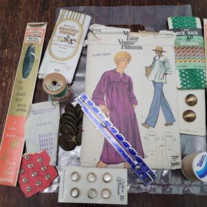 May include: Assortment of sewing supplies including buttons, thread, zippers, measuring tape, and a pattern for a dress. The pattern is for an easy Vogue pattern and includes instructions for making a dress with a long sleeve and a round neckline.
