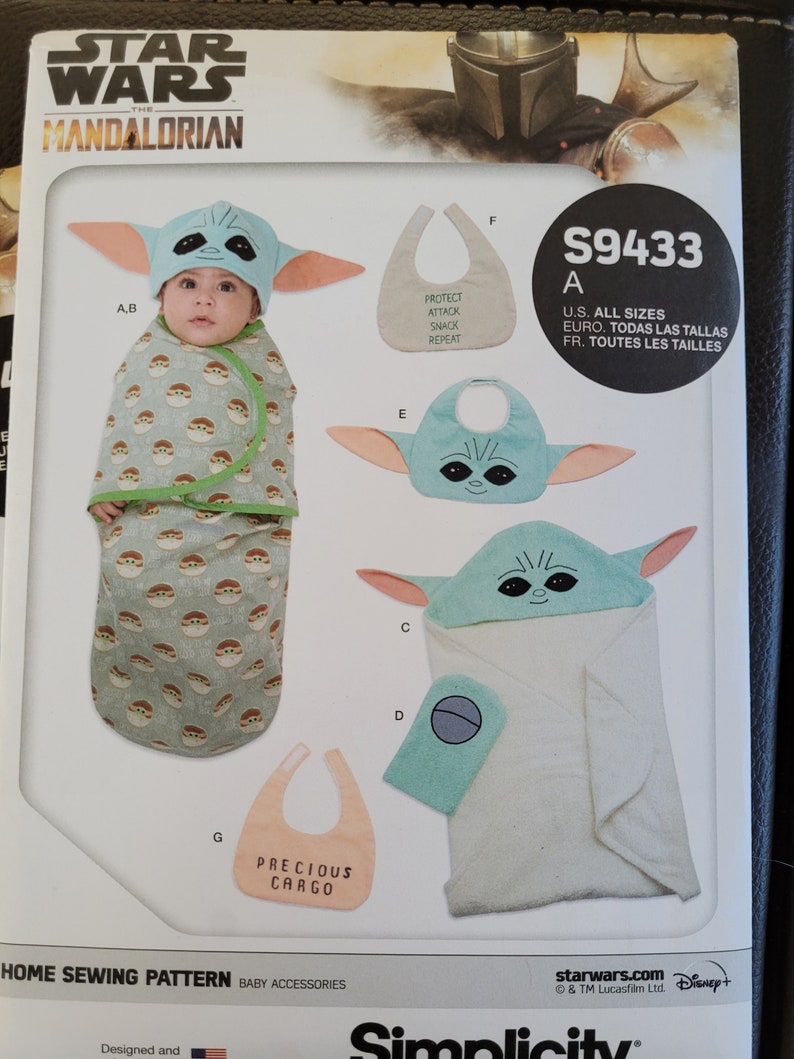 May include: A sewing pattern for baby accessories featuring a character from the Star Wars: The Mandalorian TV series. The pattern includes a hooded towel, a bib, and a sleeping bag. The pattern is labeled "S9433" and includes instructions for all sizes.