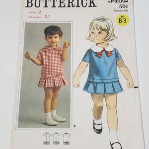 May include: A vintage sewing pattern for a girl's dress. The pattern is from Butterick and is number 3452. The pattern is for size 2 and has a bust measurement of 21 inches. The pattern is for a dress with a ruffled skirt and a Peter Pan collar. The pattern is illustrated with two drawings of girls wearing the dress.