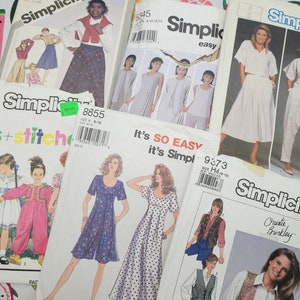 May include: A collection of vintage sewing patterns featuring various designs for women and children. The patterns are from Simplicity and include designs for dresses, skirts, tops, and jumpsuits. The patterns are in various colors and feature different styles and sizes.