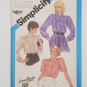 May include: A sewing pattern for a blouse with a bow tie, puff sleeves, and a button-up front. The pattern is from Simplicity and is endorsed by Leona Rocha. The pattern number is 6495.