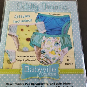 May include: A set of four different styles of baby training pants, including a swim diaper. The training pants are made of colorful fabric with various patterns, including dinosaurs and flowers. The package includes instructions and patterns for making the training pants. The text on the package reads "Totally Trainers", "4 Styles Included!" and "Babyville Boutique".