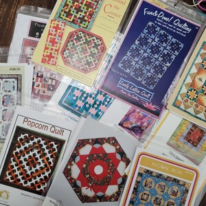 May include: A collection of quilting patterns featuring various designs, including "Daisy Cakes", "Popcorn Quilt", "Fun & Done! Quilting", "Lively Lattice Quilt", "Time - October Sky", and "Floral Box".