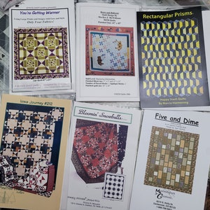 May include: Six quilting pattern designs for various quilt projects. The patterns are printed on white paper with colorful images of the finished quilts. The titles of the patterns are "You're Getting Warmer", "Iowa Journey #212", "Bloomin' Snowballs", "Rectangular Prisms", "Five and Dime", and "Beans and Balloons".