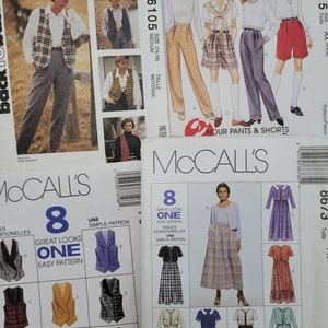 May include: Four different McCall's sewing patterns featuring various clothing designs. The patterns include a vest, pants, shorts, and dresses. The patterns are labeled with the numbers 6105, 7815, 80/3, and 8. The patterns are all for women's clothing.