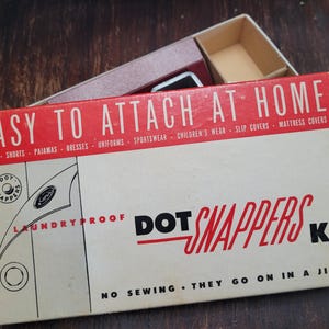May include: Vintage Dot Snappers Kit box with red and white text. The box reads "Easy to Attach at Home" and lists various clothing items. The box is open, revealing a small container inside.