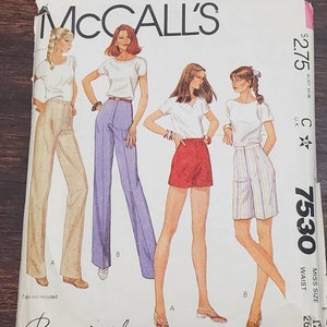 May include: McCall's sewing pattern number 7530 for a women's top and pants. The pattern includes three different views: a white top with brown pants, a white top with purple pants, and a red top with red shorts. The pattern is for sizes 12 to 26 1/2.