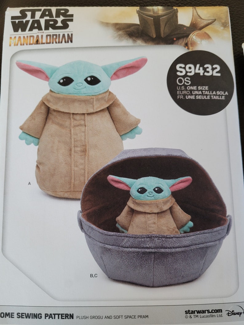 May include: A sewing pattern for a plush Grogu toy and a soft space pram from Star Wars: The Mandalorian. The pattern includes instructions for making a plush toy of the character Grogu, also known as "The Child", and a pram for the toy to sit in. The pattern is labeled "S9432 OS" and includes instructions for making the toy in one size.