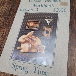 May include: A white rabbit cross stitch pattern with a basket of tulips and a heart. The pattern is titled "Spring Time" and is from the Thread Benders Workbook Lesson 3. The price is $2.00.