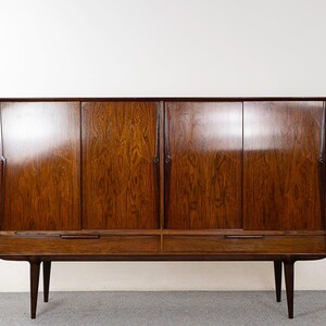 May include: A mid-century modern wooden cabinet with four doors and two drawers. The cabinet is made of dark wood with a glossy finish. It has a rectangular shape and sits on four tapered legs.