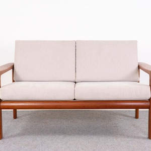 May include: A two-seater sofa with a light beige cushion and a wooden frame. The sofa has a mid-century modern design, with a rectangular shape and armrests. The wooden frame is a warm brown color, and the cushions are a neutral tone.
