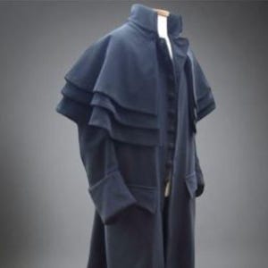 May include: A dark navy blue long coat featuring a high collar and a multi-layered capelet design over the shoulders. The coat has a front button closure, long sleeves with cuffs, and a full-length silhouette that extends to the lower legs.
