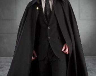 Könnte beinhalten: Ein schwarzer Umhang mit passendem Anzug. Der Umhang hat einen breiten Kragen und einen goldfarbenen Knopf. Der Anzug umfasst ein weißes Hemd und eine schwarze Krawatte. Das Outfit ist formell und elegant.