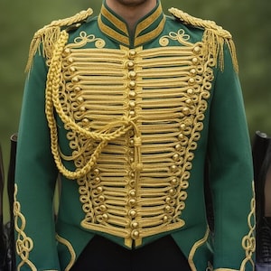Könnte beinhalten: Eine grüne Militärjacke mit goldenen Verzierungen, darunter Schulterklappen, Besatz und dekorative Zöpfe. Die Jacke hat einen hohen Kragen und goldene Knöpfe. Schwarze Stiefel sind im Hintergrund aufgereiht.