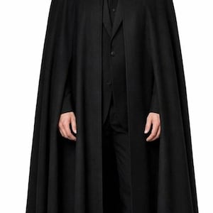 Könnte beinhalten: Ein langer, schwarzer Umhang mit breitem Kragen, getragen über einem schwarzen Anzug. Der Umhang ist bodenlang und hat ein fließendes Design. Das Outfit ist formell und elegant.