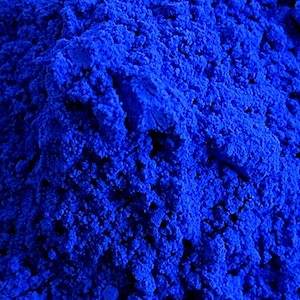 以下が含まれることがあります： 鮮やかな濃い青色の粉末の山をクローズアップ。質感は粒状でわずかに不均一で、光と影のバリエーションが奥行きを生み出しています。色は一貫しており、単一の顔料または染料を示唆しています。