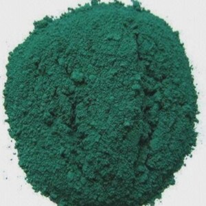 Puede incluir: Un mont&oacute;n de polvo finamente molido, de color verde azulado oscuro. El polvo tiene un aspecto texturizado y granulado, con variaciones de tono que crean luces y sombras. La forma general es un mont&iacute;culo redondeado sobre un fondo blanco.