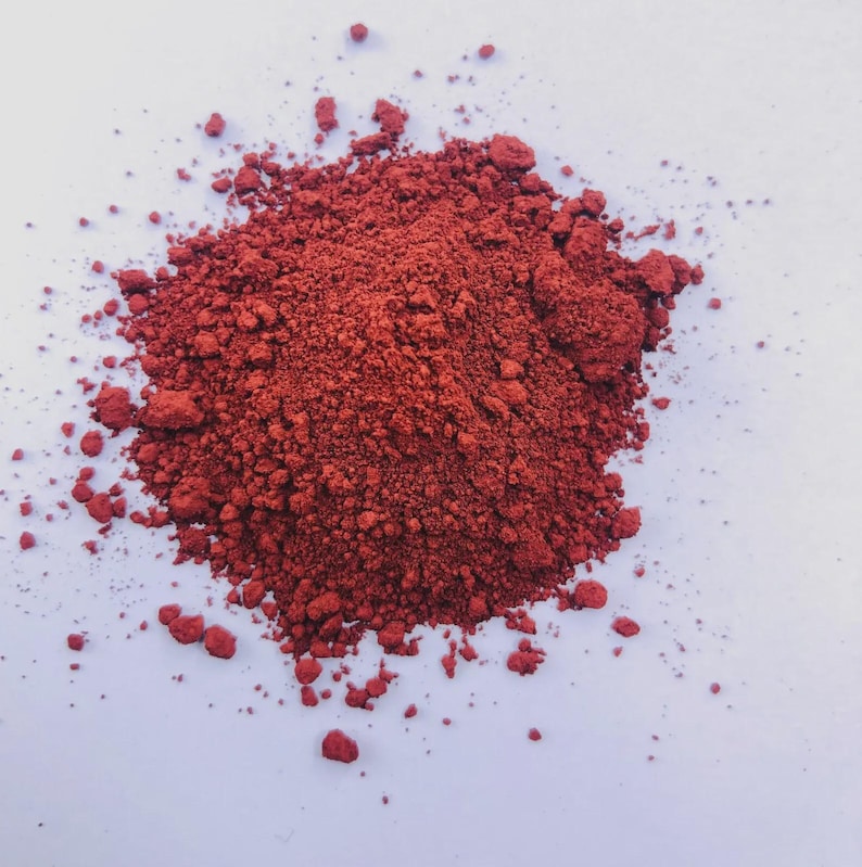 Puede incluir: Un mont&oacute;n de polvo de pigmento rojo intenso y finamente molido, esparcido sobre una superficie blanca. El polvo tiene una textura granular y diferentes tonos de rojo. La imagen est&aacute; bien iluminada, resaltando la textura.