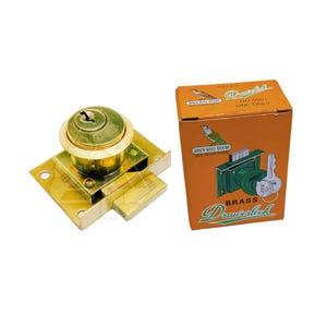 May include: A brass drawer lock with a key and a matching orange box. The lock is gold-colored and has a round keyhole. The box features a bird illustration and the words "Drawerlock" and "Brass".