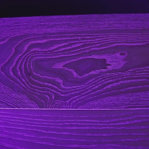 May include: A close-up of a purple wooden surface with visible wood grain patterns. The wood has a rich, deep purple color, with lighter shades highlighting the grain's texture. The surface is divided by a horizontal line.