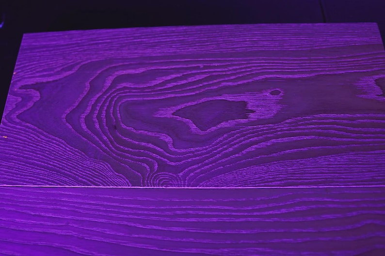 May include: A close-up of a purple wooden surface with visible wood grain patterns. The wood has a rich, deep purple color, with lighter shades highlighting the grain's texture. The surface is divided by a horizontal line.