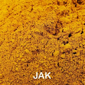 May include: Close-up of a pile of finely ground, bright yellow powder. The texture is granular and uneven, with small peaks and valleys. The word "JAK" is printed in white at the bottom of the image.