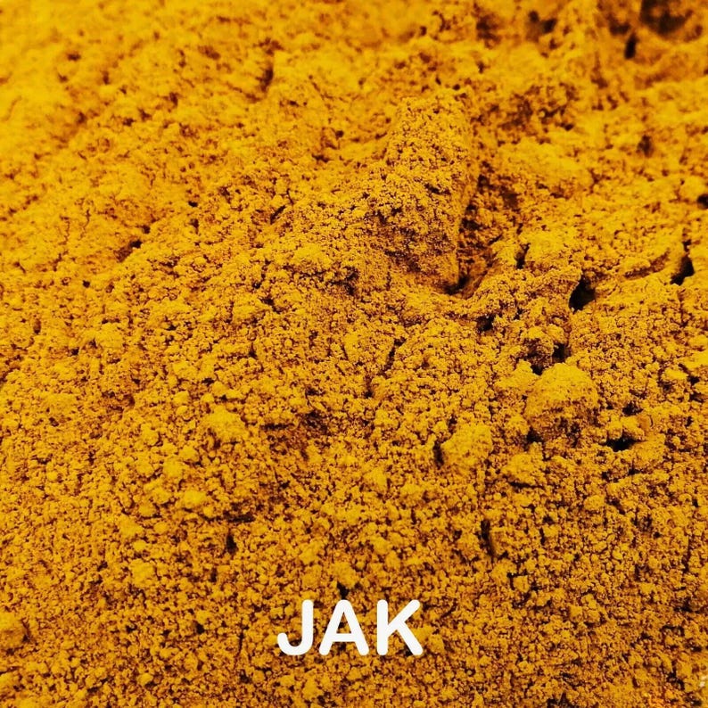 May include: Close-up of a pile of finely ground, bright yellow powder. The texture is granular and uneven, with small peaks and valleys. The word "JAK" is printed in white at the bottom of the image.