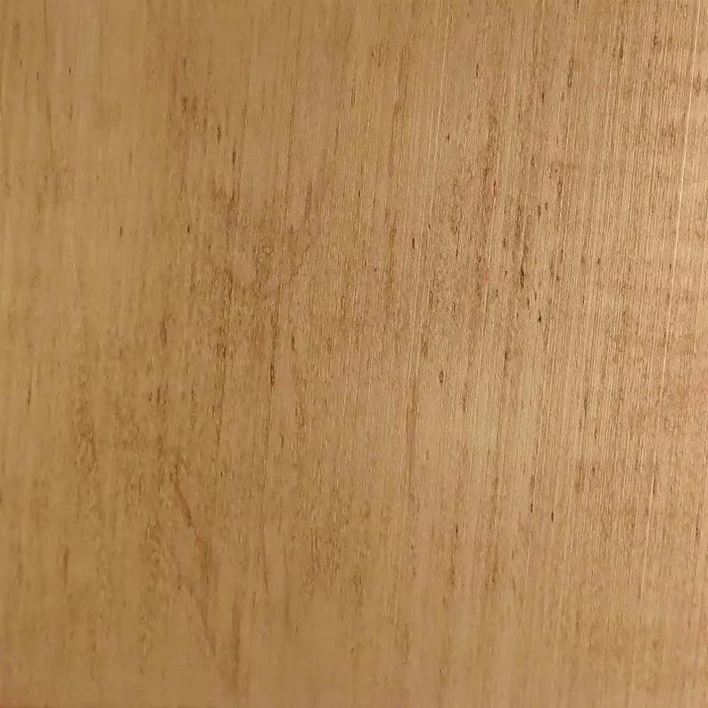 May include: Close-up of a light brown wooden surface with visible grain and subtle color variations. The wood has a natural, warm tone, with vertical lines and small dark spots adding texture. The surface appears smooth and well-finished.