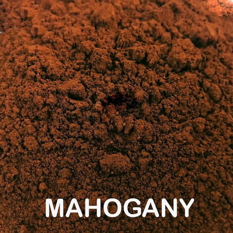 May include: Close-up of a pile of finely ground, dark brown powder. The powder has a textured, granular appearance. The word "MAHOGANY" is displayed in white, bold letters at the bottom of the image.