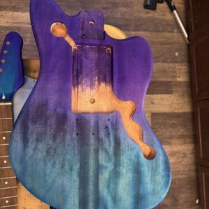 Peut inclure: Corps de guitare partiellement assembl&eacute; avec une finition d&eacute;grad&eacute;e dans les tons de bleu et de violet. Le corps pr&eacute;sente des d&eacute;coupes pour les micros, le chevalet et le manche. Le manche et la t&ecirc;te sont &eacute;galement visibles, avec une finition bleue.