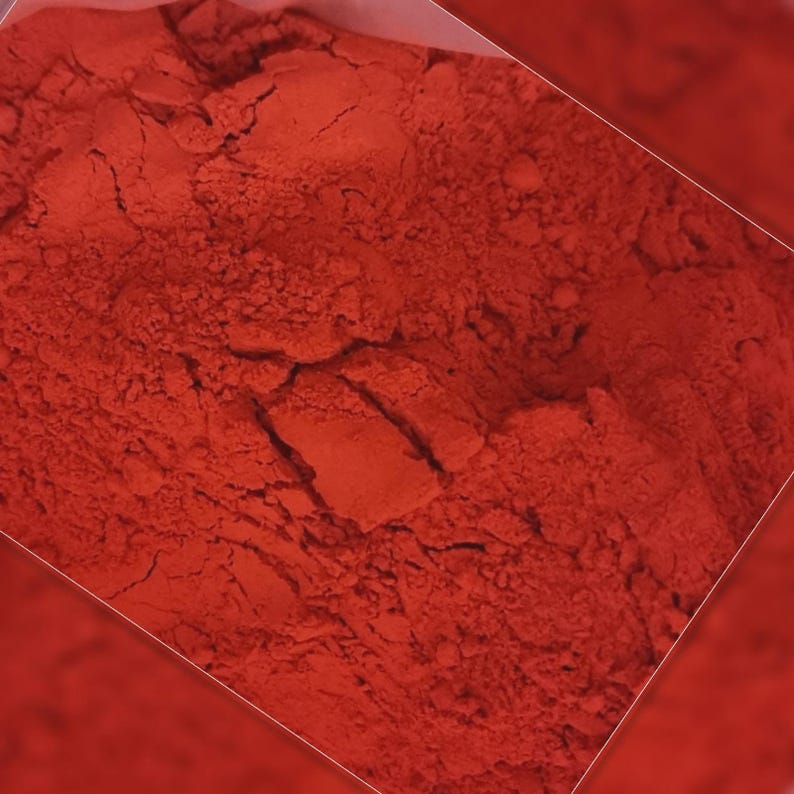 Puede incluir: Primer plano de un polvo rojo vibrante, probablemente un pigmento o tinte. El polvo tiene una apariencia fina y texturizada con gr&aacute;nulos visibles y sutiles variaciones de tono. La imagen est&aacute; bien iluminada, resaltando el rico color y la textura del material.