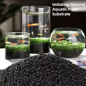 Puede incluir: Tres acuarios de vidrio de varias formas y tamaños, cada uno con agua, peces pequeños y plantas acuáticas. El texto "Imitating Natural Aquatic Plant Substrate" es visible. Un montón de sustrato negro está en primer plano.